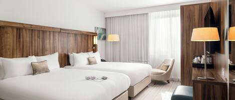 Habitación de hotel con dos camas, un escritorio, una silla y un ventanal grande con cortinas.