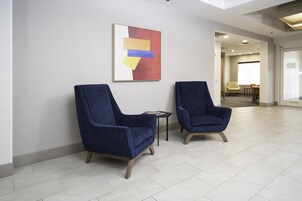 Duas poltronas azuis em um hall moderno com um quadro geométrico na parede.