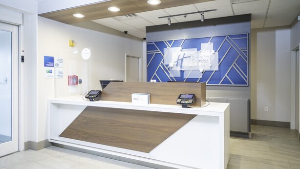 A reception desk with a modern design, a blue accent wall, and a wooden panel. - Holiday Inn Express Hotel & Suites Atlanta Johns Creek by IHG (Suwanee)