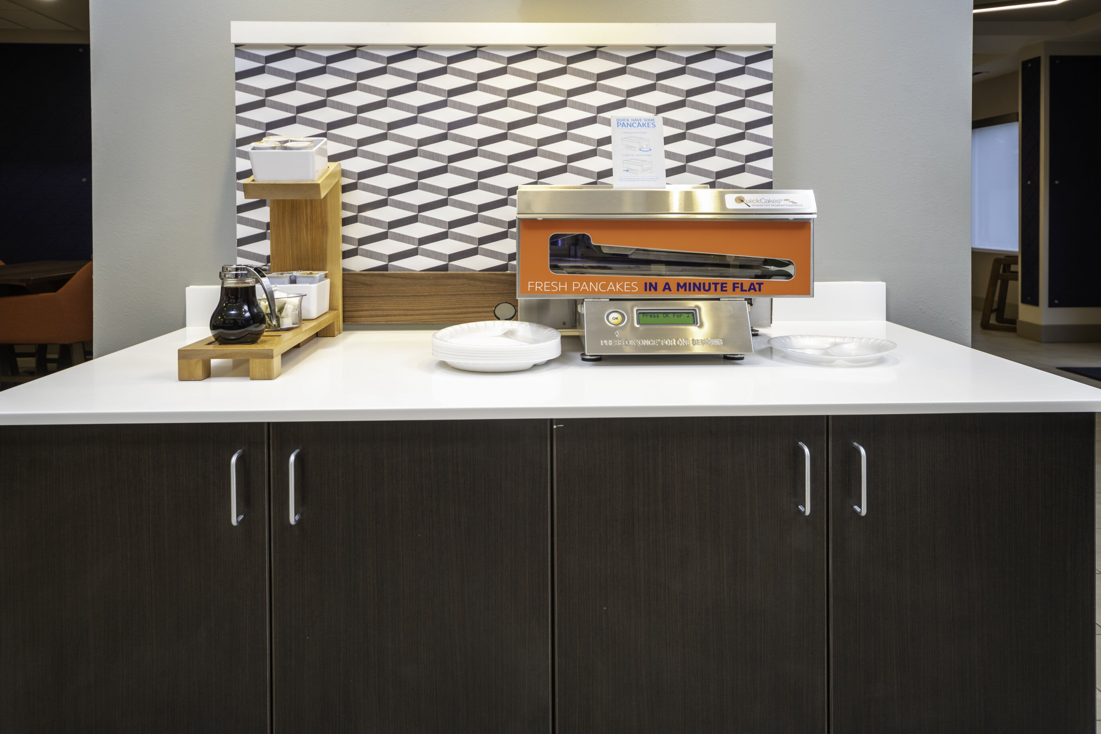 A breakfast station with a coffee machine, a sign for pancakes, and a tray with a pitcher and cups.