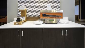 A breakfast station with a coffee machine, a sign for pancakes, and a tray with a pitcher and cups.