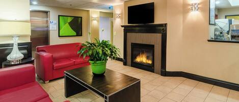 A modern living room with a red sofa, a black coffee table, a green plant, a fireplace, and a flat-screen TV mounted above it.