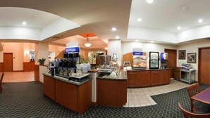 A hotel lobby with a reception desk, coffee machines, a self-service breakfast area, and a seating area with a table and chairs. - Holiday Inn Express & Suites Vinita by IHG (Vinita)