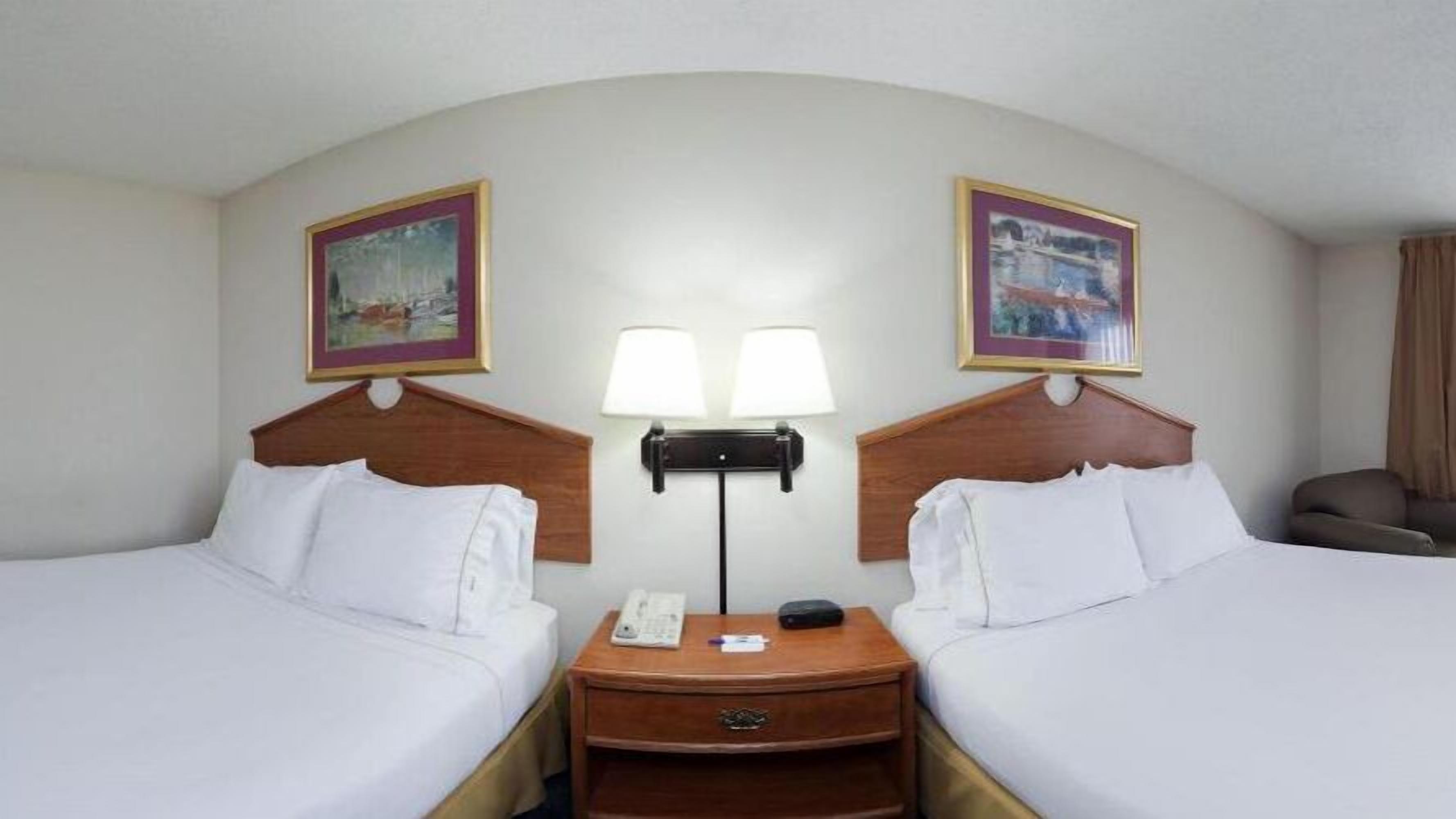 Ein Hotelzimmer mit zwei Betten, einem Nachttisch mit Telefon und Lampe sowie zwei gerahmten Bildern an der Wand.