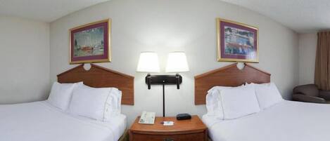 Une chambre d’hôtel avec deux lits, une table de chevet avec un téléphone et une lampe, et deux tableaux encadrés au mur.