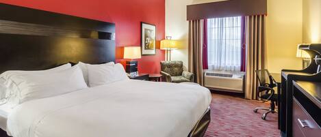 A hotel room with a large bed, a desk, a chair, a lamp, and a window with curtains.