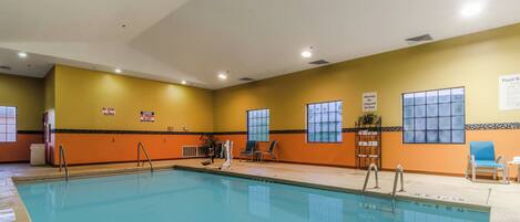 An indoor swimming pool with safety signs, a lifeguard chair, and a seating area with chairs and a table.