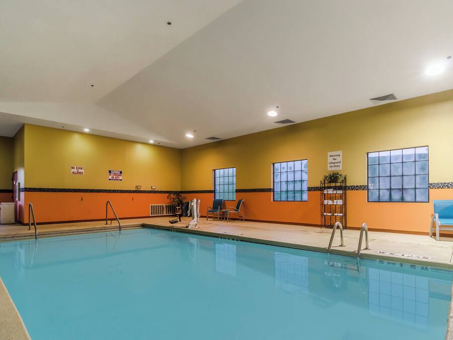 Una piscina interior amb senyals de seguretat, una cadira de socorrista i una zona amb seients, cadires i una taula.