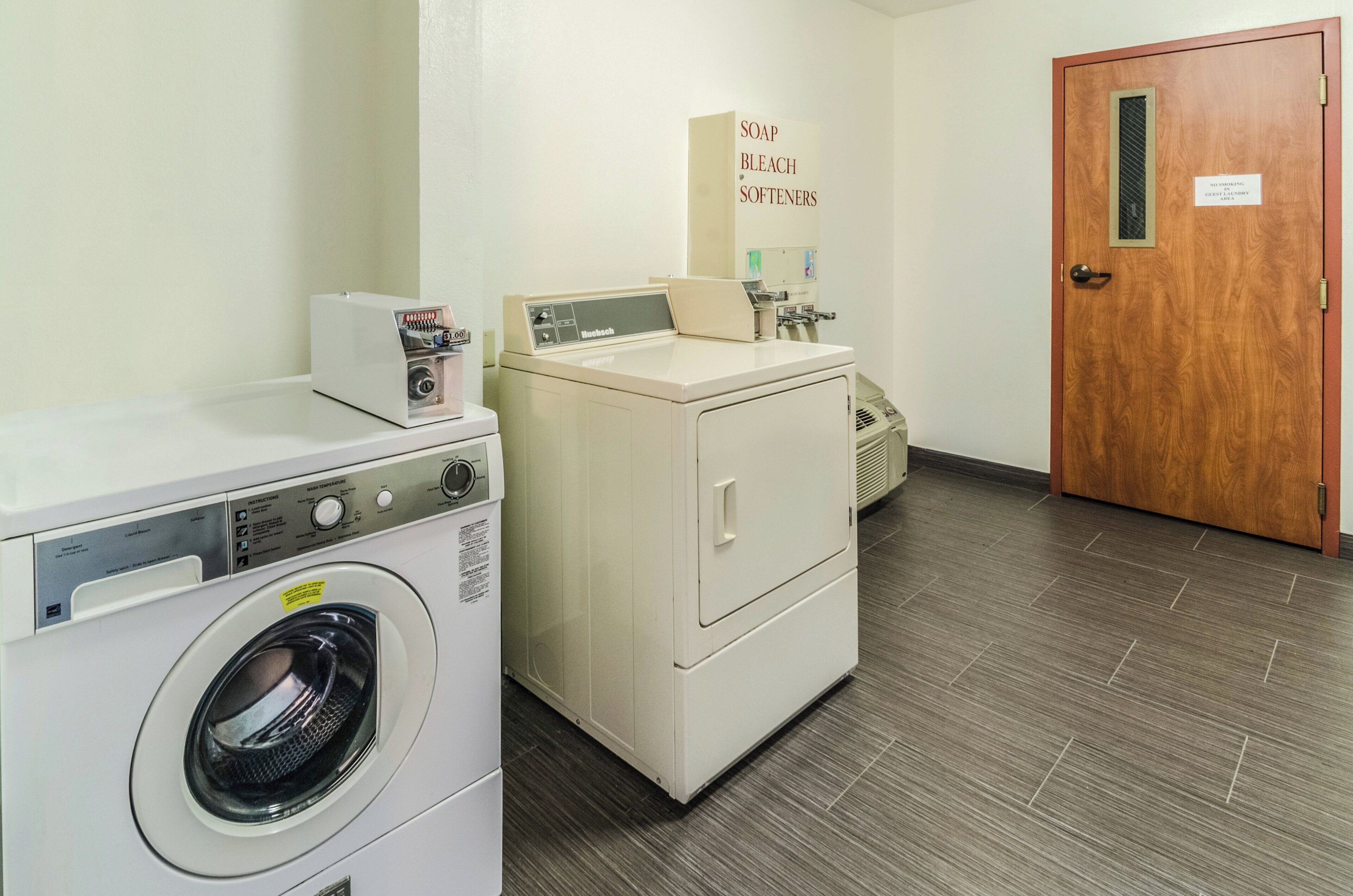 A laundry area with a front-loading washing machine, a dryer, and a wall-mounted soap and bleach dispenser.