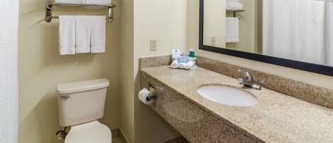 A bathroom with a toilet, sink, and mirror. There are towels on a rack and a bottle of hand soap on the counter.