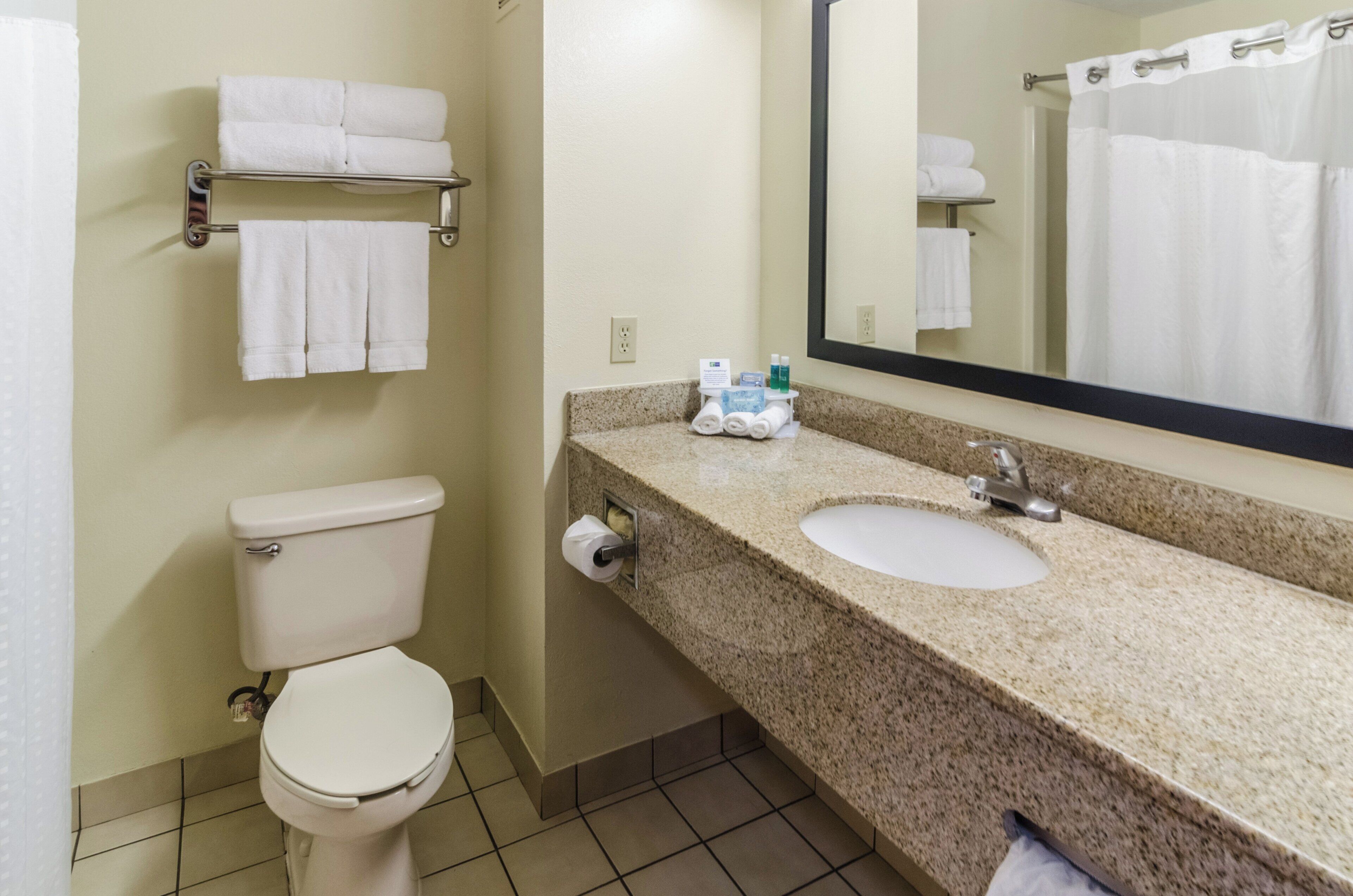 A bathroom with a toilet, sink, and mirror. There are towels on a rack and toiletries on the sink.
