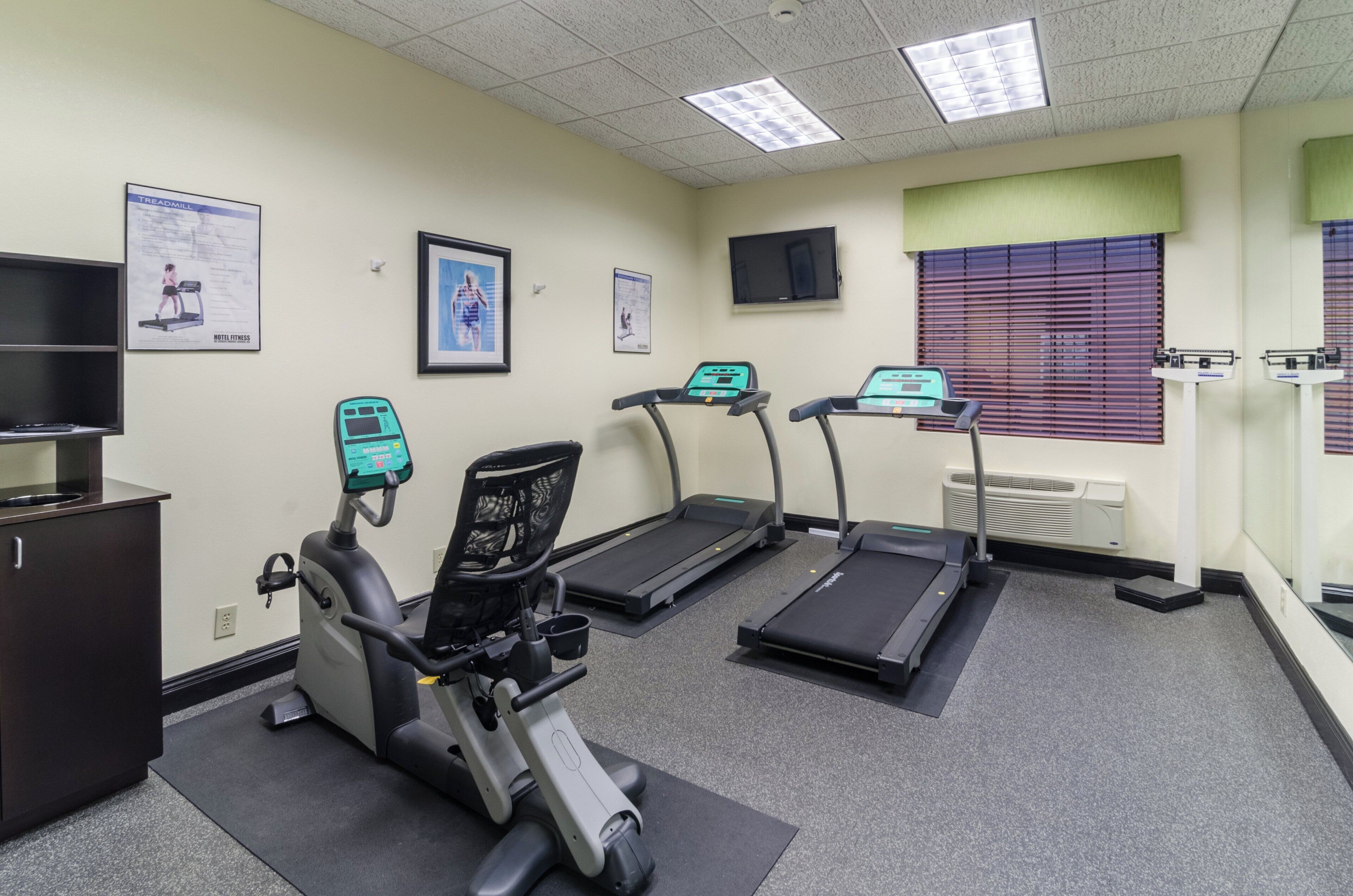 Un gimnasio con cintas de correr, una bicicleta estática y un televisor montado en la pared.