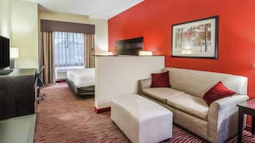 A hotel room with a bed, a sofa, a TV, and a painting on the wall.