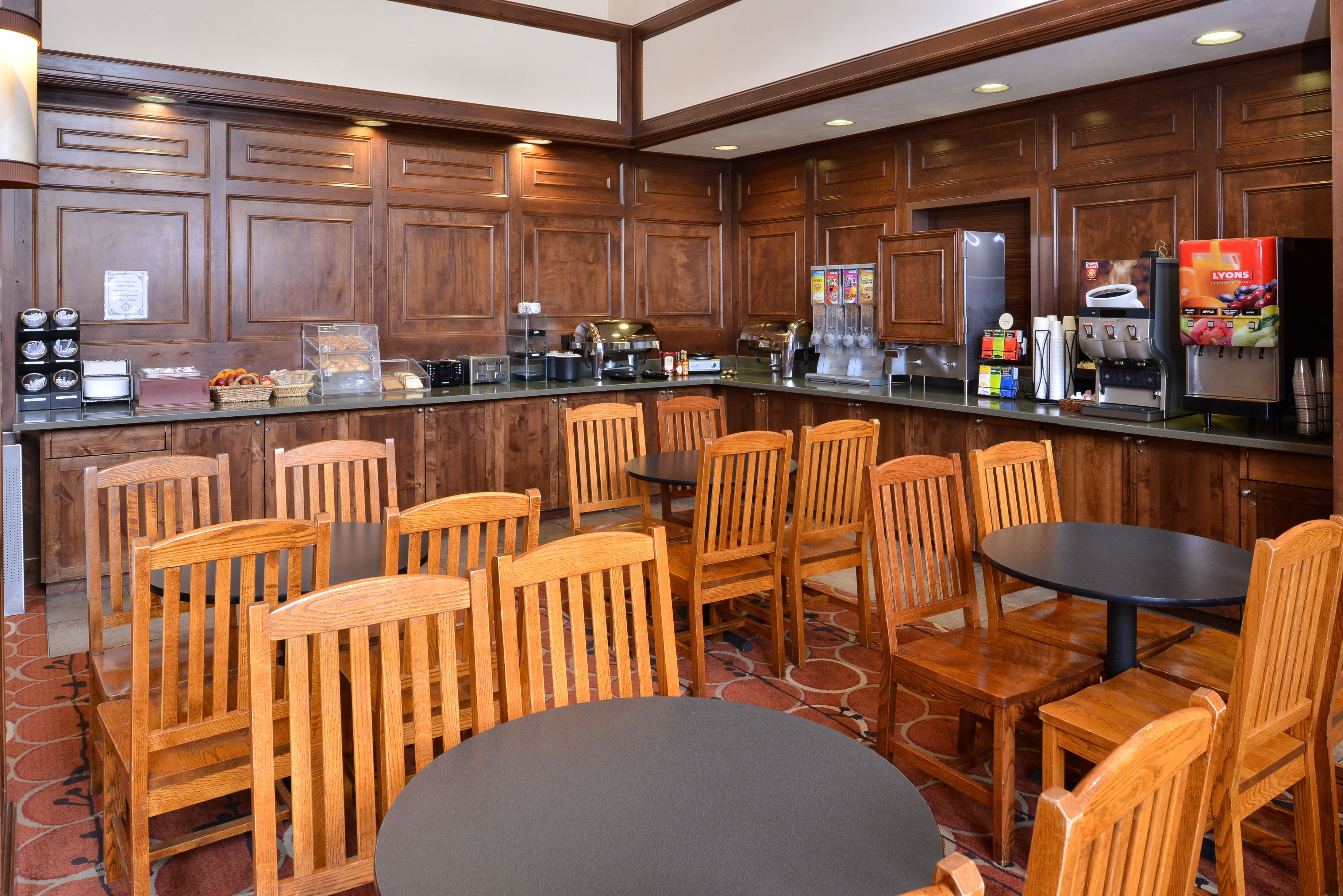 A hotel kitchen with wooden paneling, a coffee station, and seating for guests.