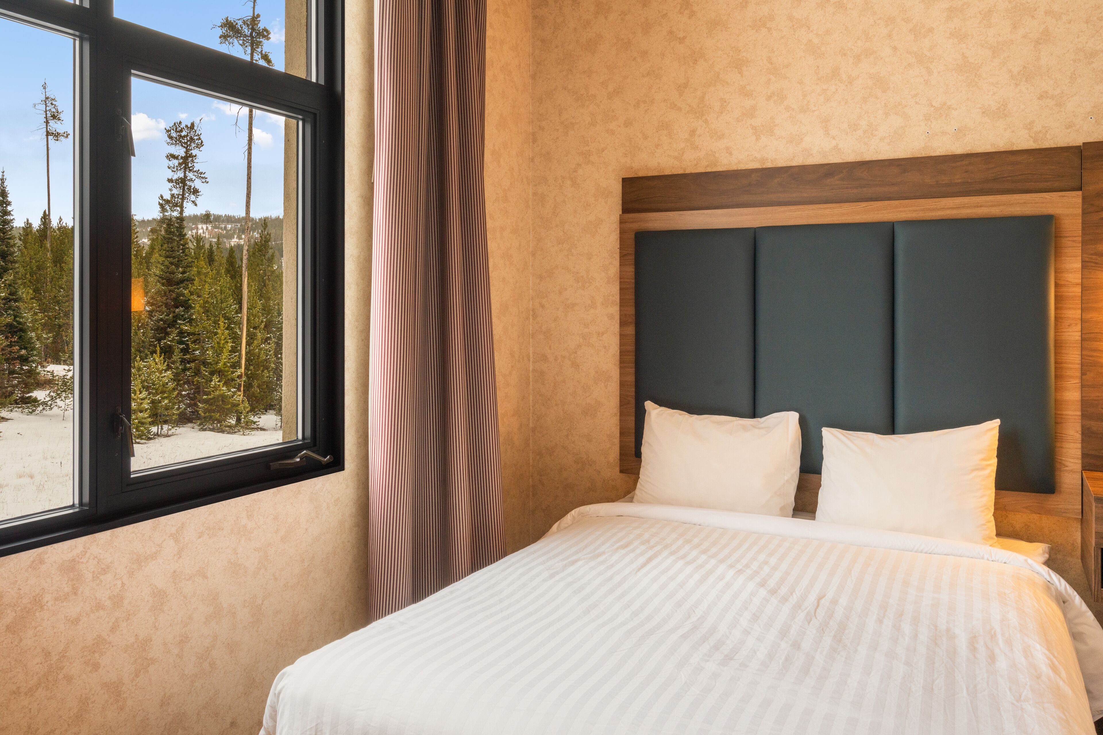 A hotel room with a large window, a bed with white bedding, and a wooden headboard.