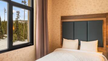 A hotel room with a large window, a bed with white bedding, and a wooden headboard.