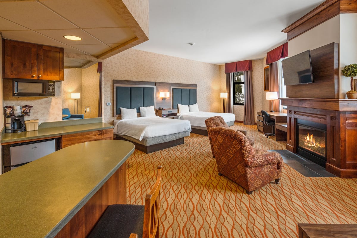 A hotel room with two beds, a sofa, a fireplace, a television, and a kitchenette.