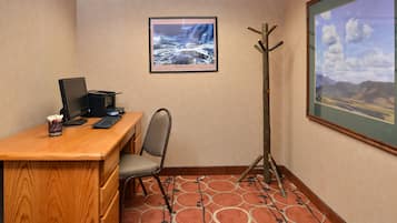A conference room with a wooden desk, a computer, a chair, a coat rack, and two framed pictures on the walls.