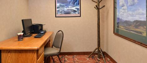 Une salle de conférence avec un bureau en bois, un ordinateur, une chaise, un porte-manteau et deux tableaux encadrés accrochés aux murs.