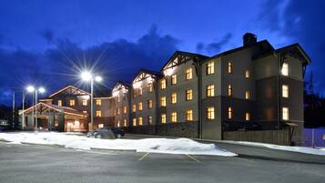 Un hotel grande de varios pisos con una entrada bien iluminada y un estacionamiento cubierto de nieve.