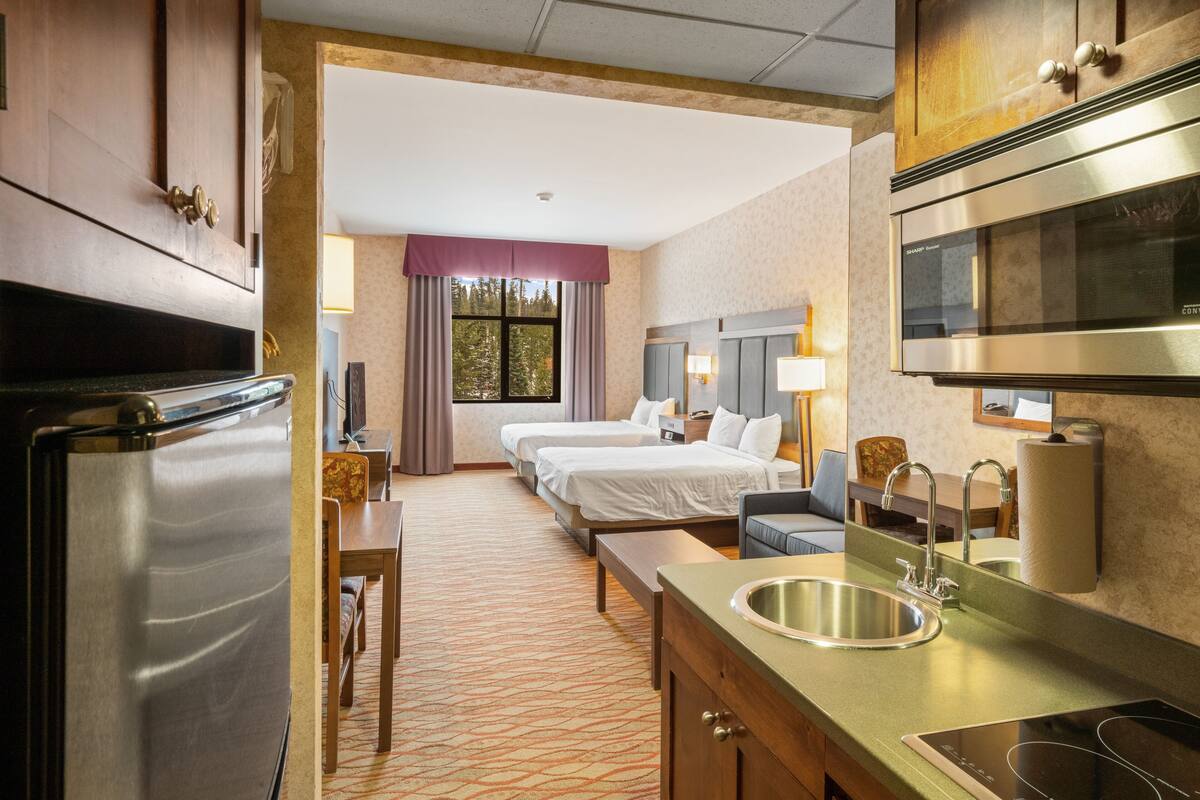 A hotel room with a kitchenette, a bed, a desk, and a bathroom.