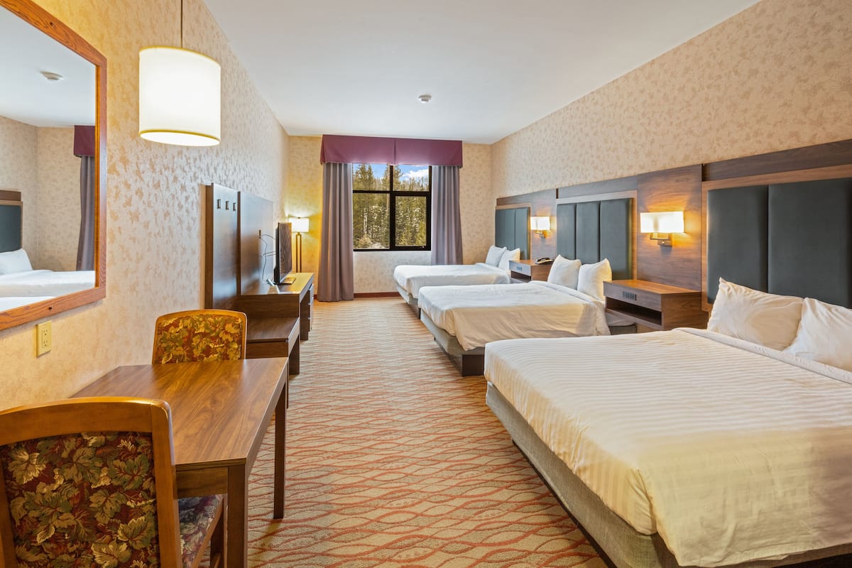 A hotel room with three beds, a desk, and a chair.