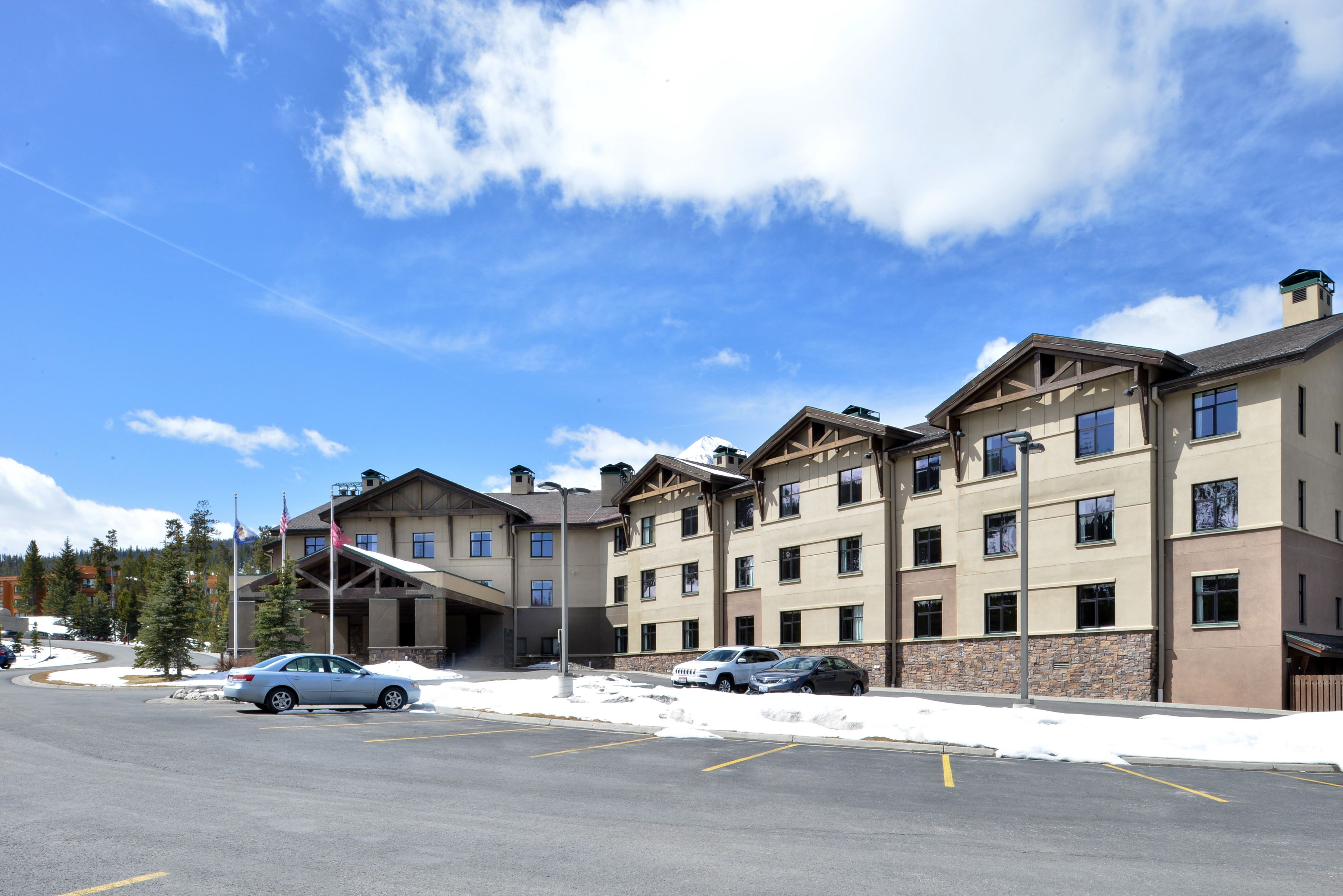 A multi-story hotel with a stone facade, multiple balconies, and a parking lot with several cars.