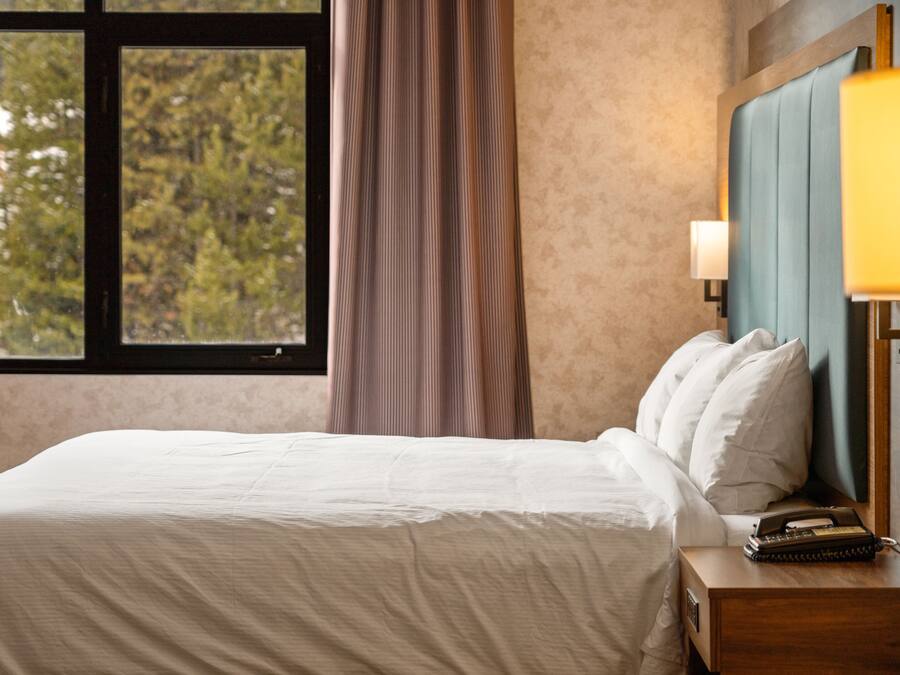 A hotel room with a bed, a nightstand, a lamp, and a window with curtains.