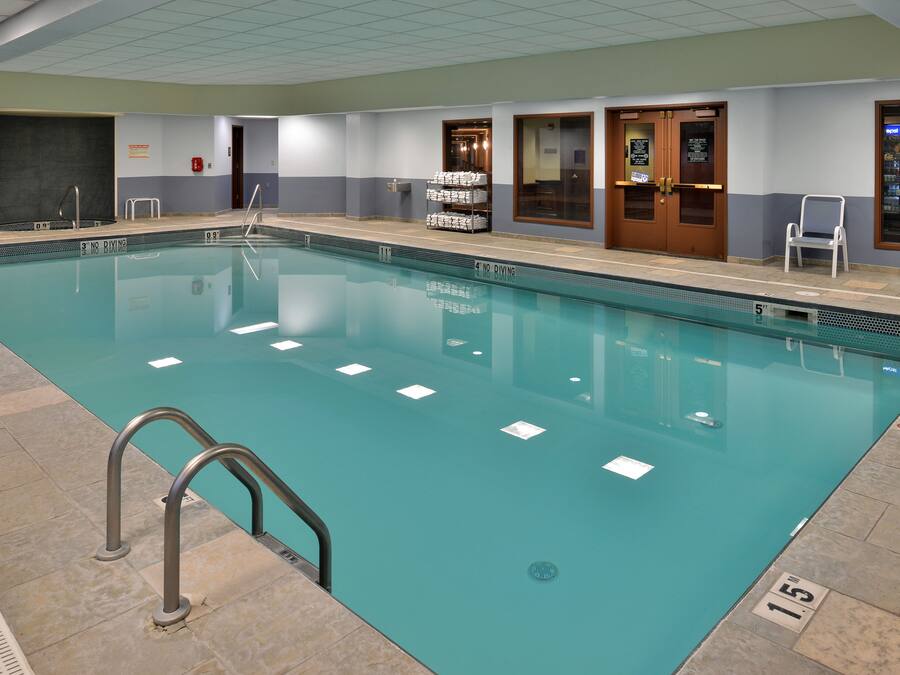 Una amplia piscina interior con marcas de carril definidas, una escalera de metal y un cartel de prohibición de saltos.