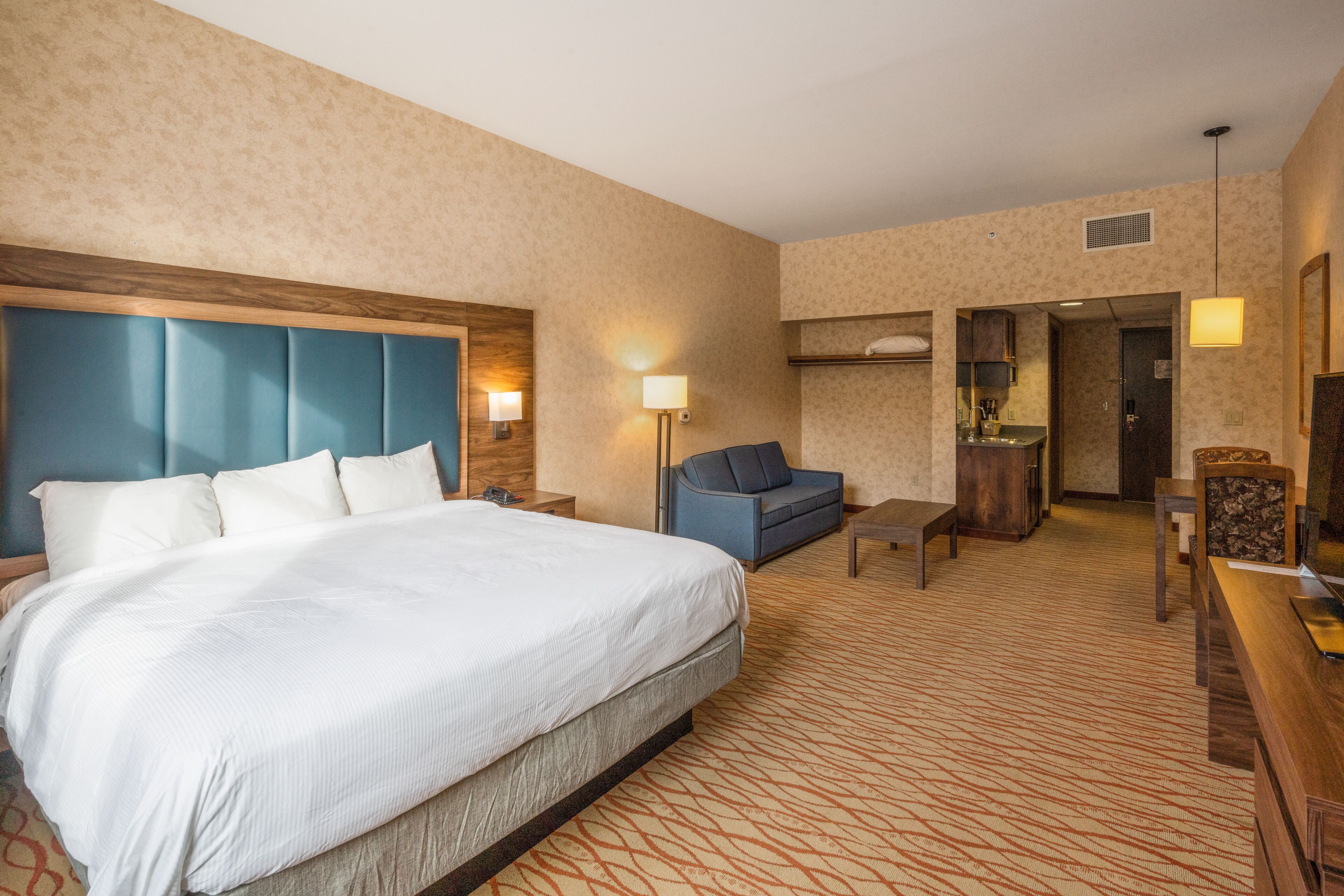 A hotel room with a large bed, a sofa, a desk, and a kitchenette.