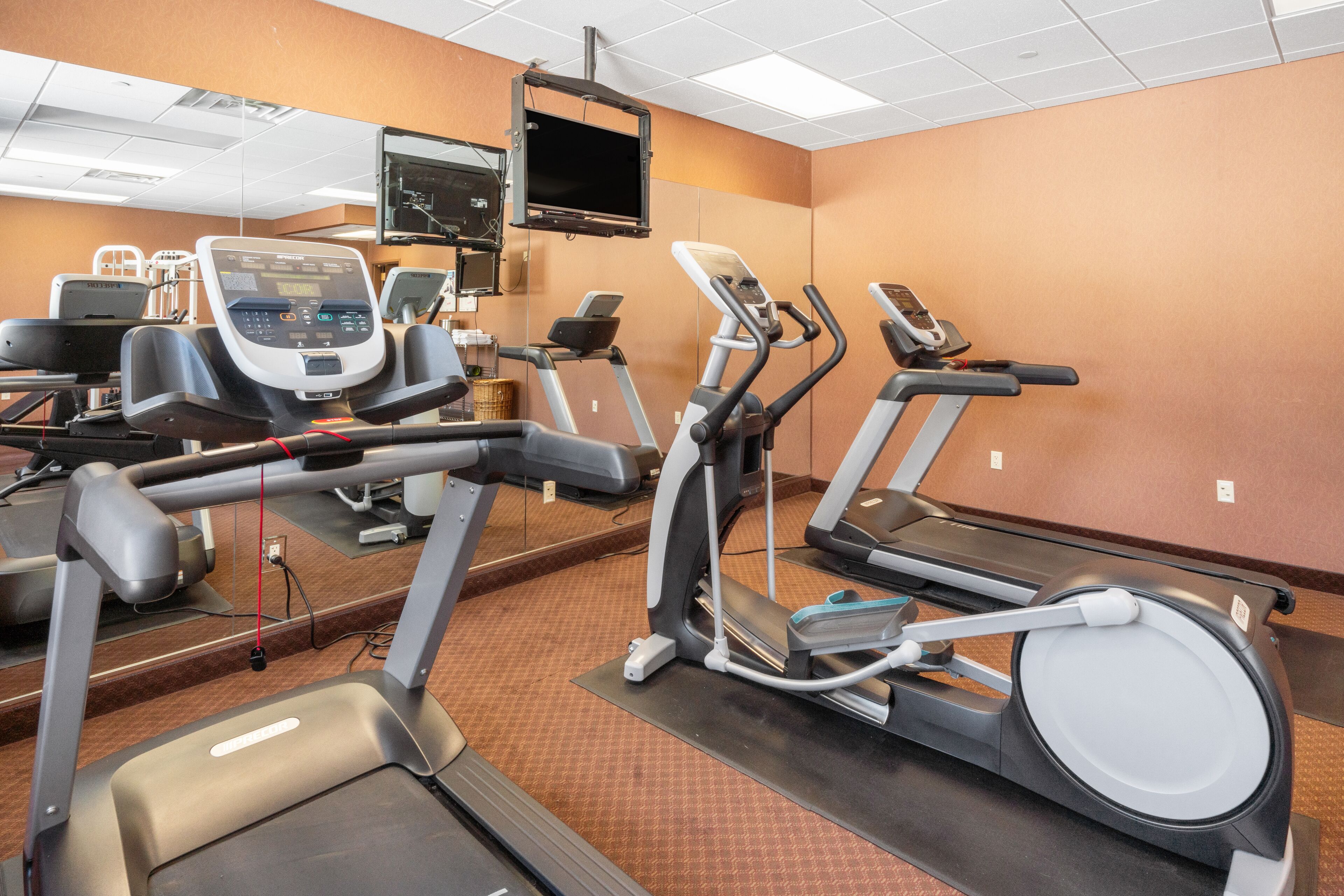 Un gimnasio equipado con cintas de correr, elípticas y un espejo grande.