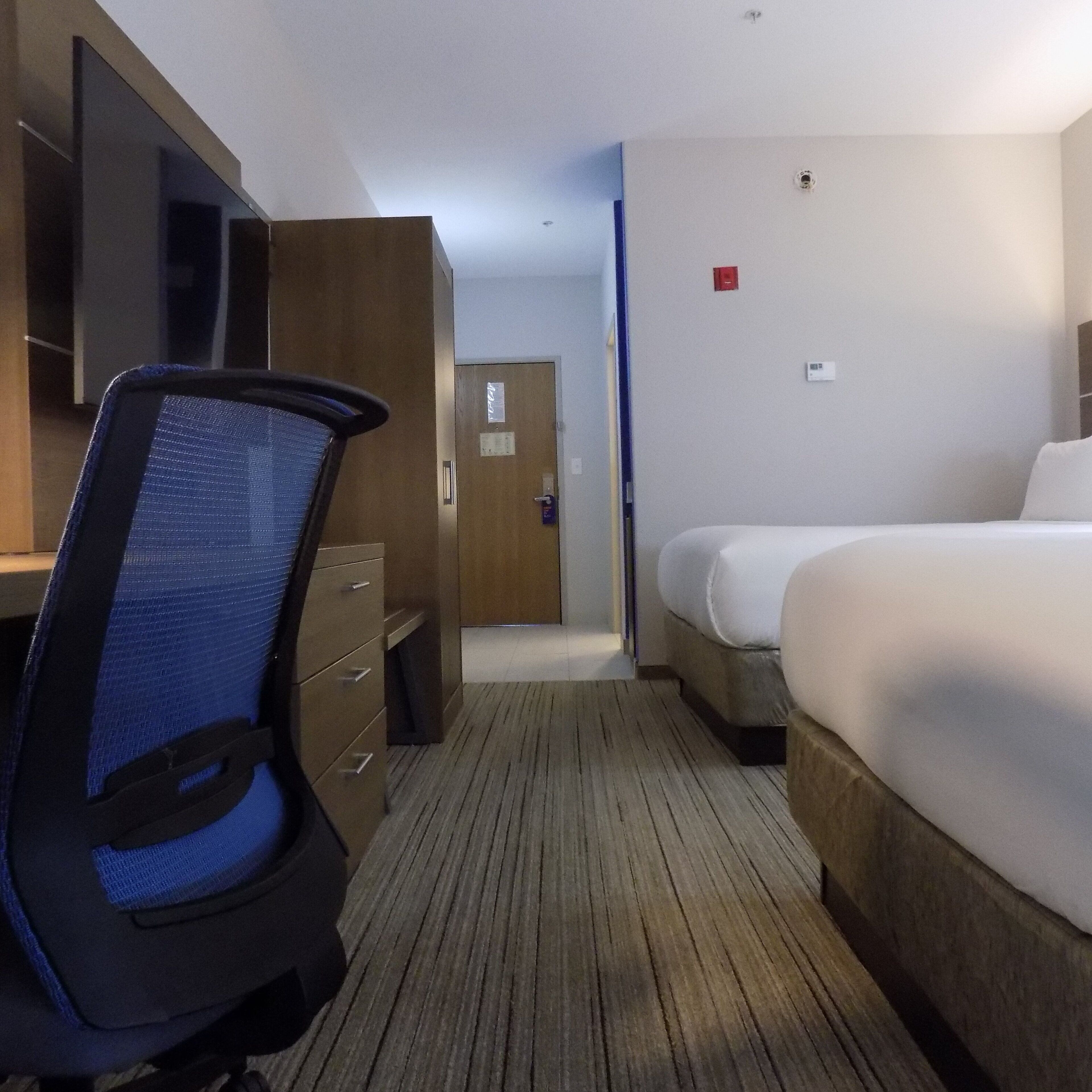 A hotel room with a bed, a desk with a chair, a wardrobe, and a door leading to another room.