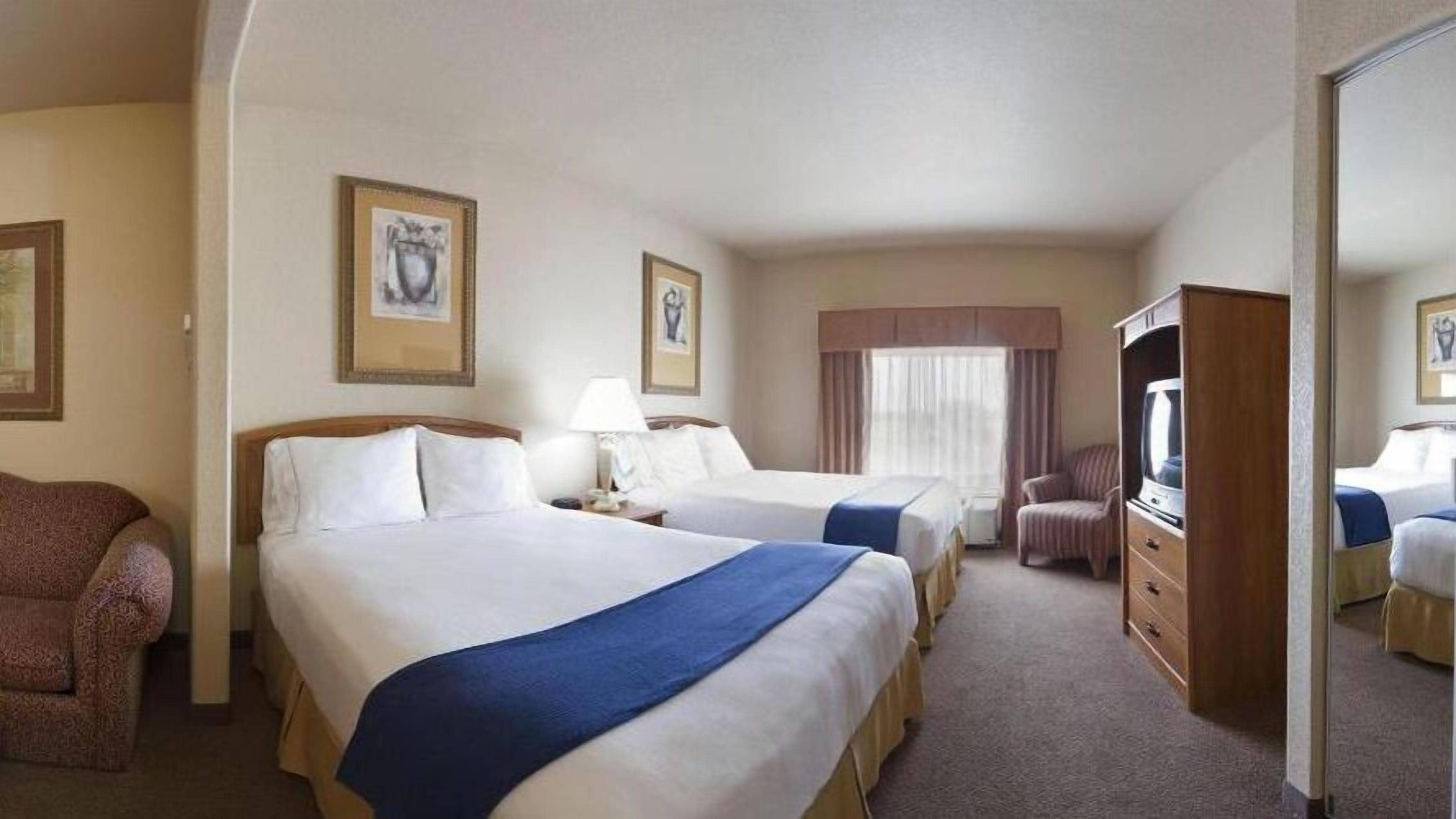 A hotel room with two beds, a TV, a chair, and a dresser.