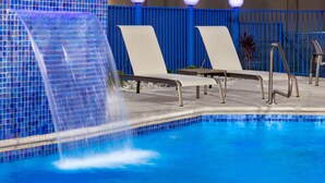 A swimming pool with a waterfall feature, lounge chairs, and a blue fence. - Holiday Inn Express Hotel & Suites Mission-McAllen Area by IHG (Mission)