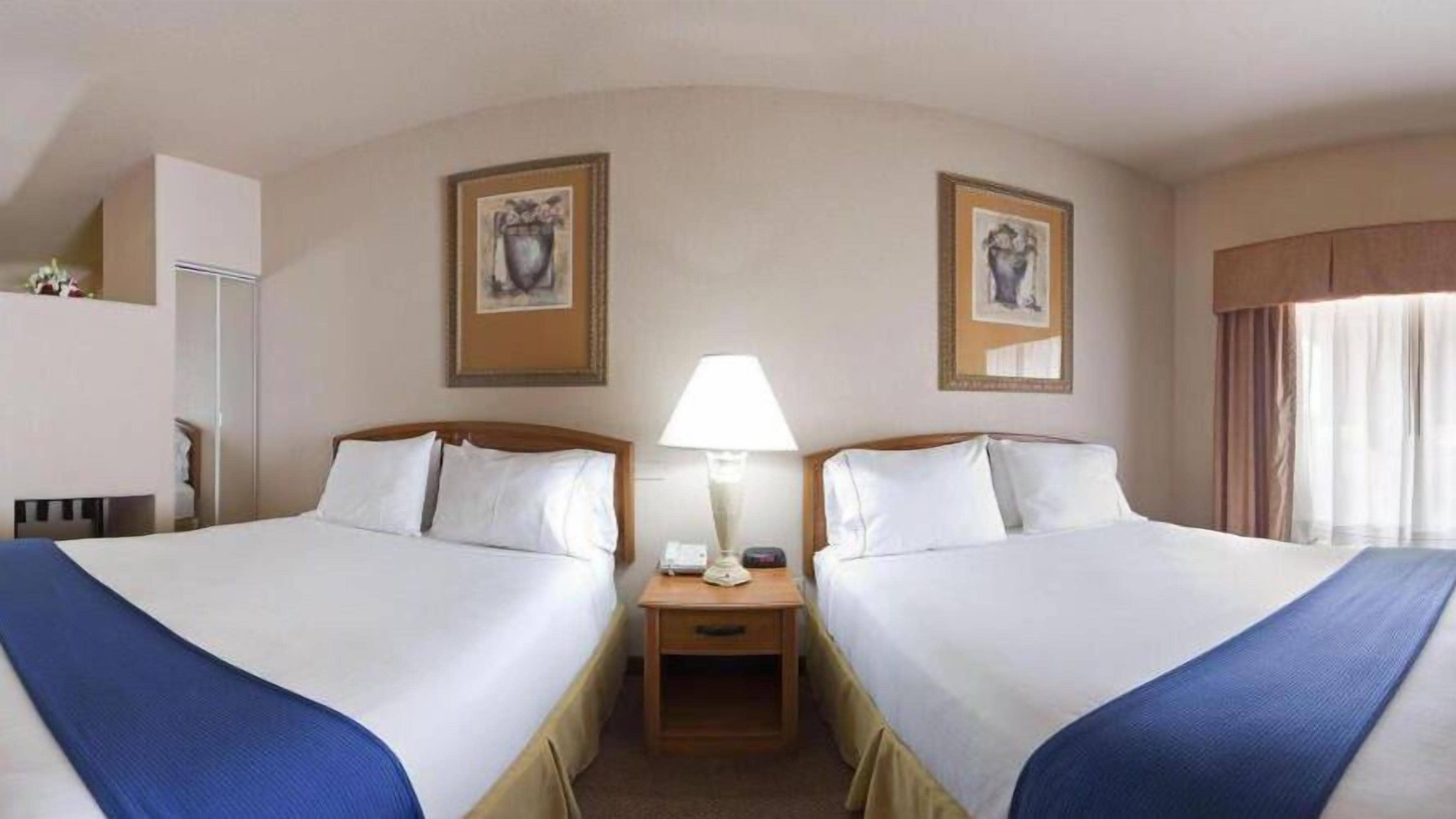 A hotel room with two beds, a nightstand with a lamp, and artwork on the walls.