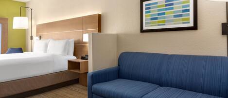 Habitación de hotel con cama, sofá azul, mesita pequeña y lámpara de pared.