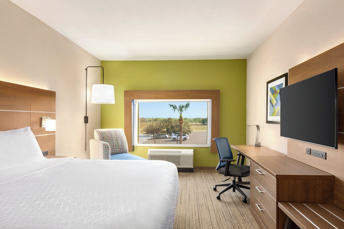 A hotel room with a large bed, a desk with a chair, a TV, and a window with a view of the outdoors.