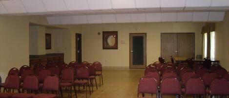Un salón de conferencias con filas de sillas rojas, un atril y un amplio ventanal.