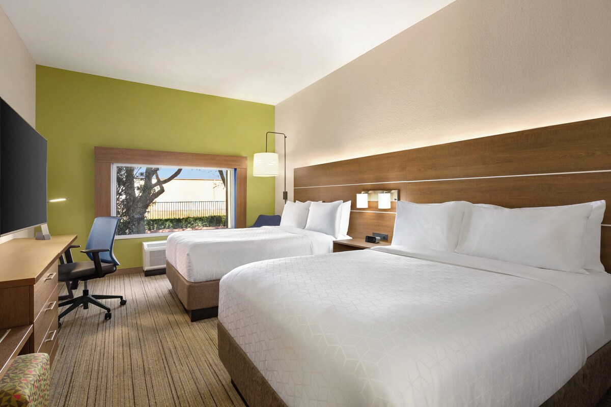 A hotel room with two beds, a desk, a chair, and a TV.
