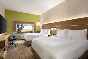 A hotel room with two beds, a desk, a chair, a TV, and a window with a view of trees.