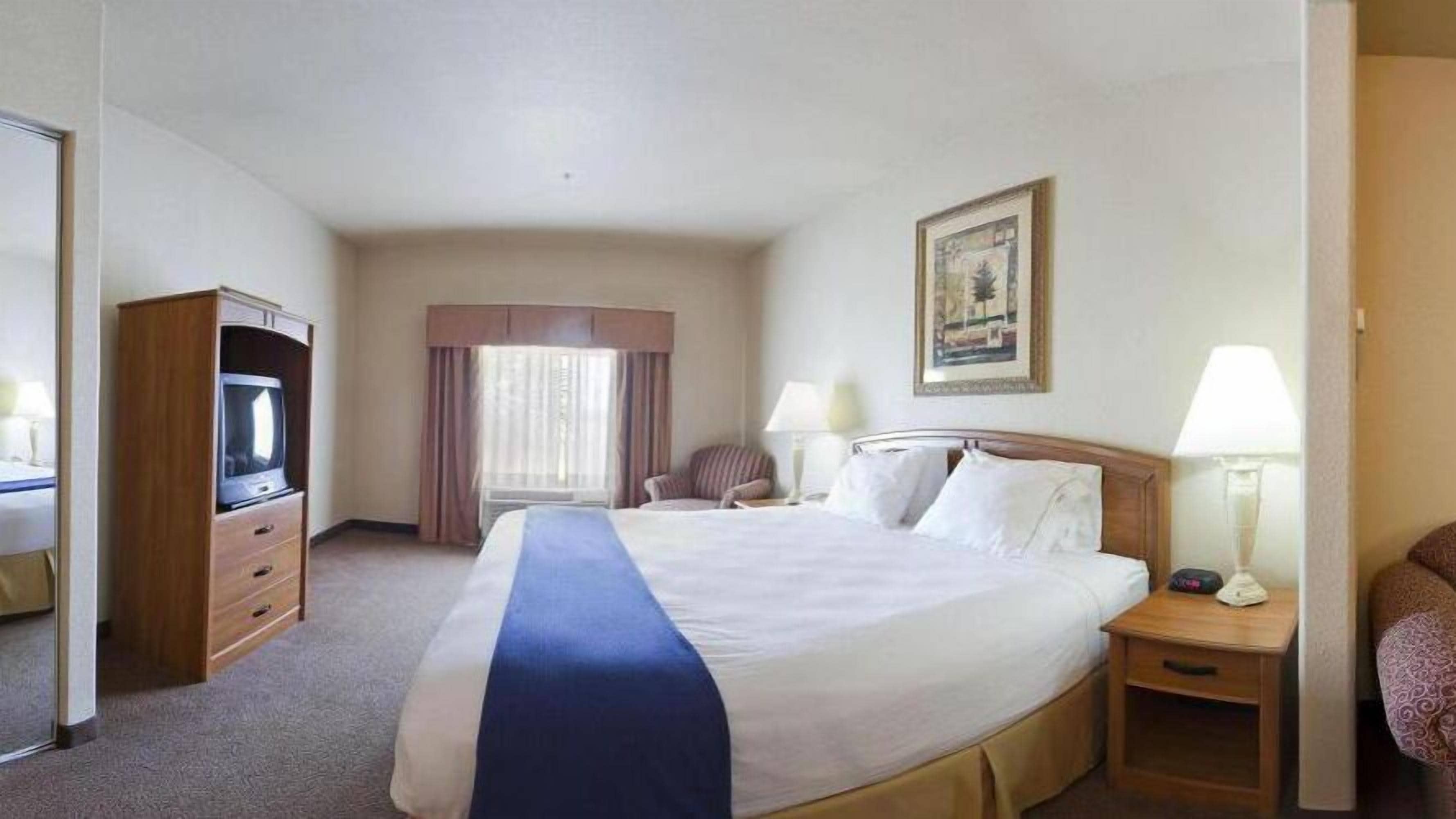 A hotel room with a large bed, a desk, a chair, a television, and a window with curtains.