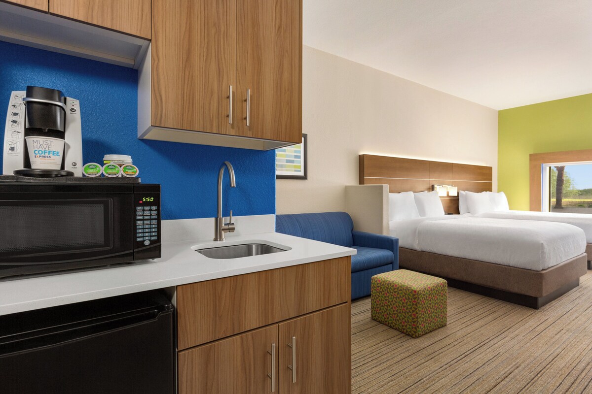 A hotel room with a kitchenette, a bed, a bedside table, and a window.