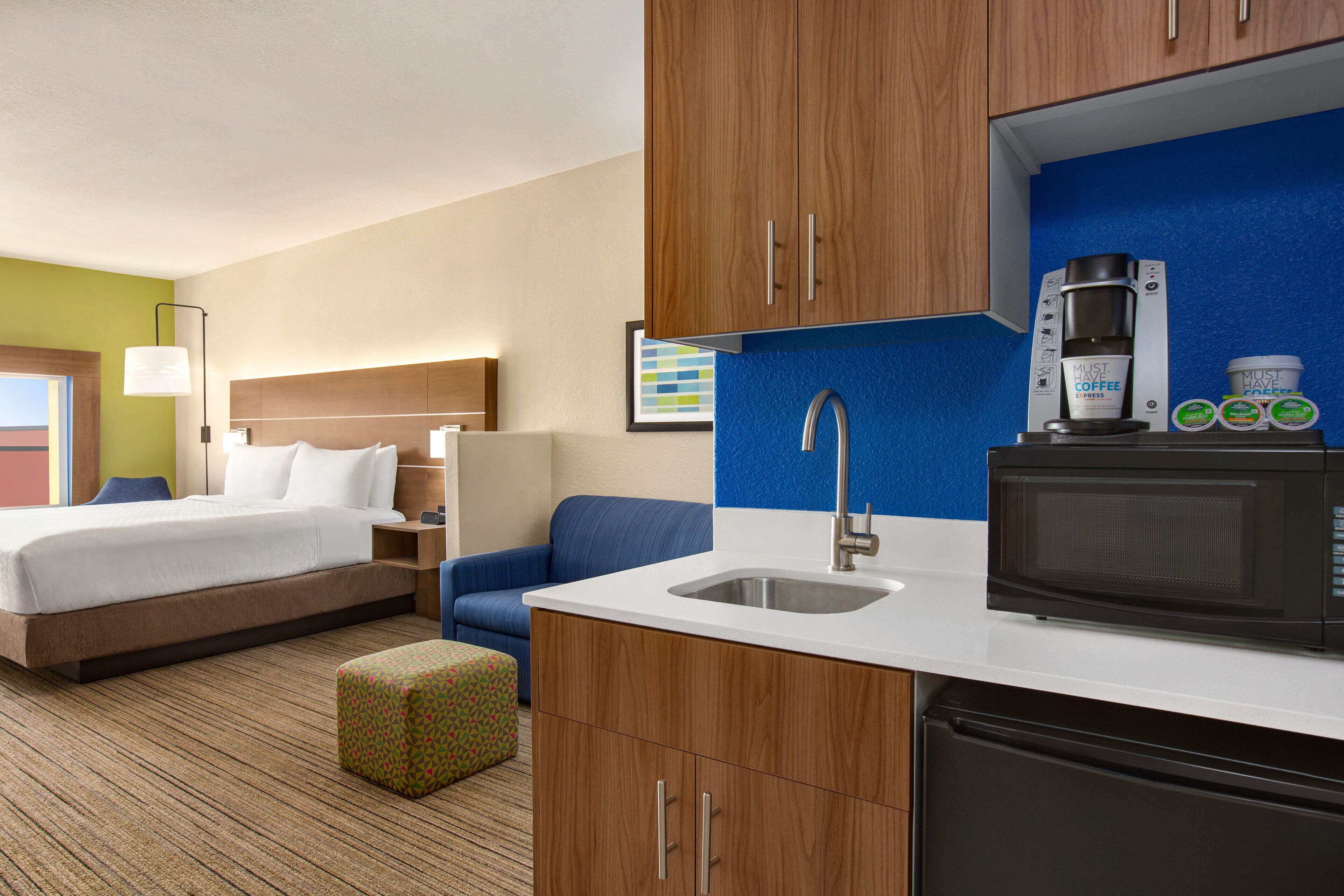 Habitación de hotel con cama, escritorio, silla, kitchenette y microondas.