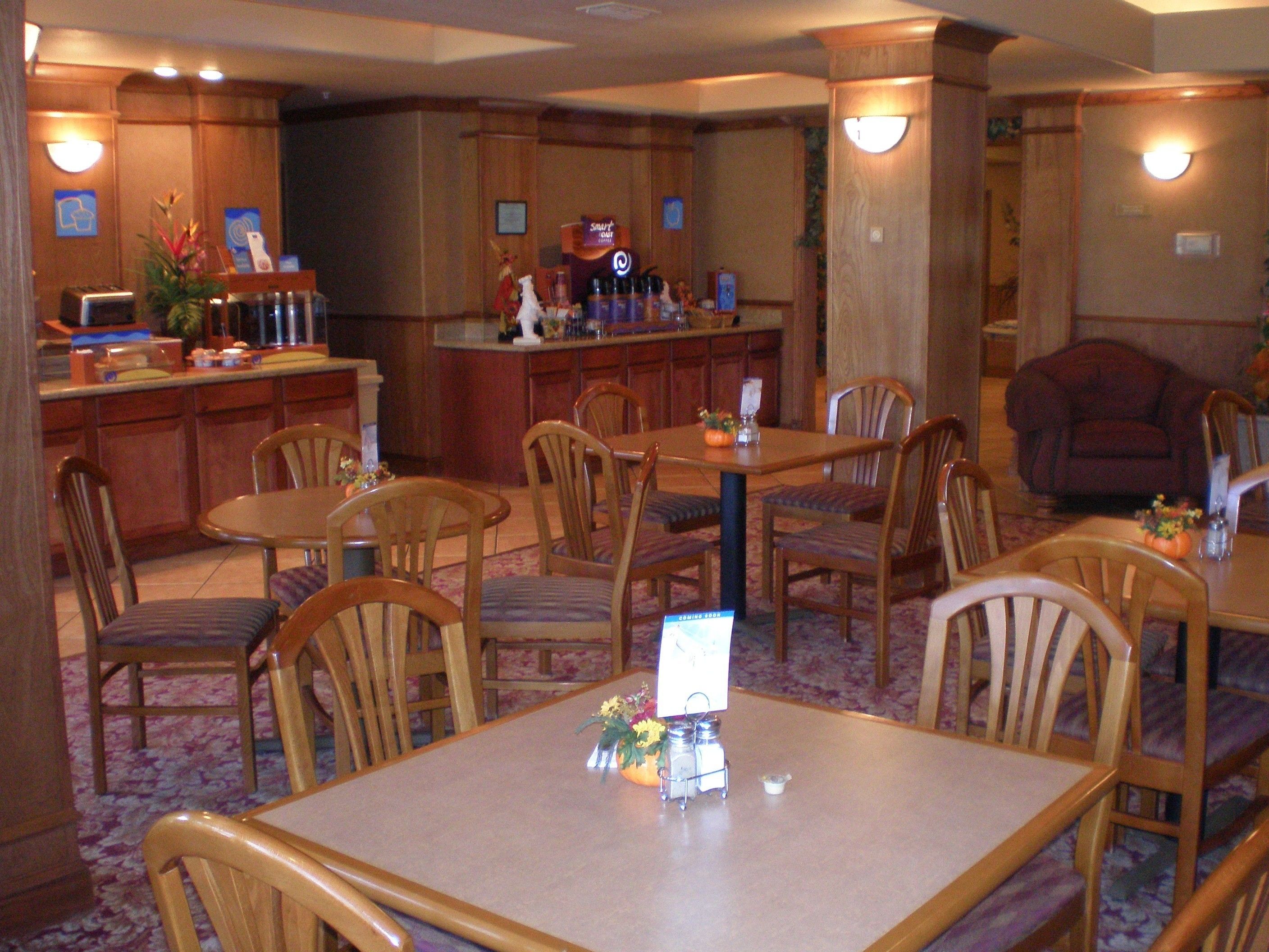 A hotel dining area with wooden tables and chairs, a bar area with a counter, and a small reception desk.