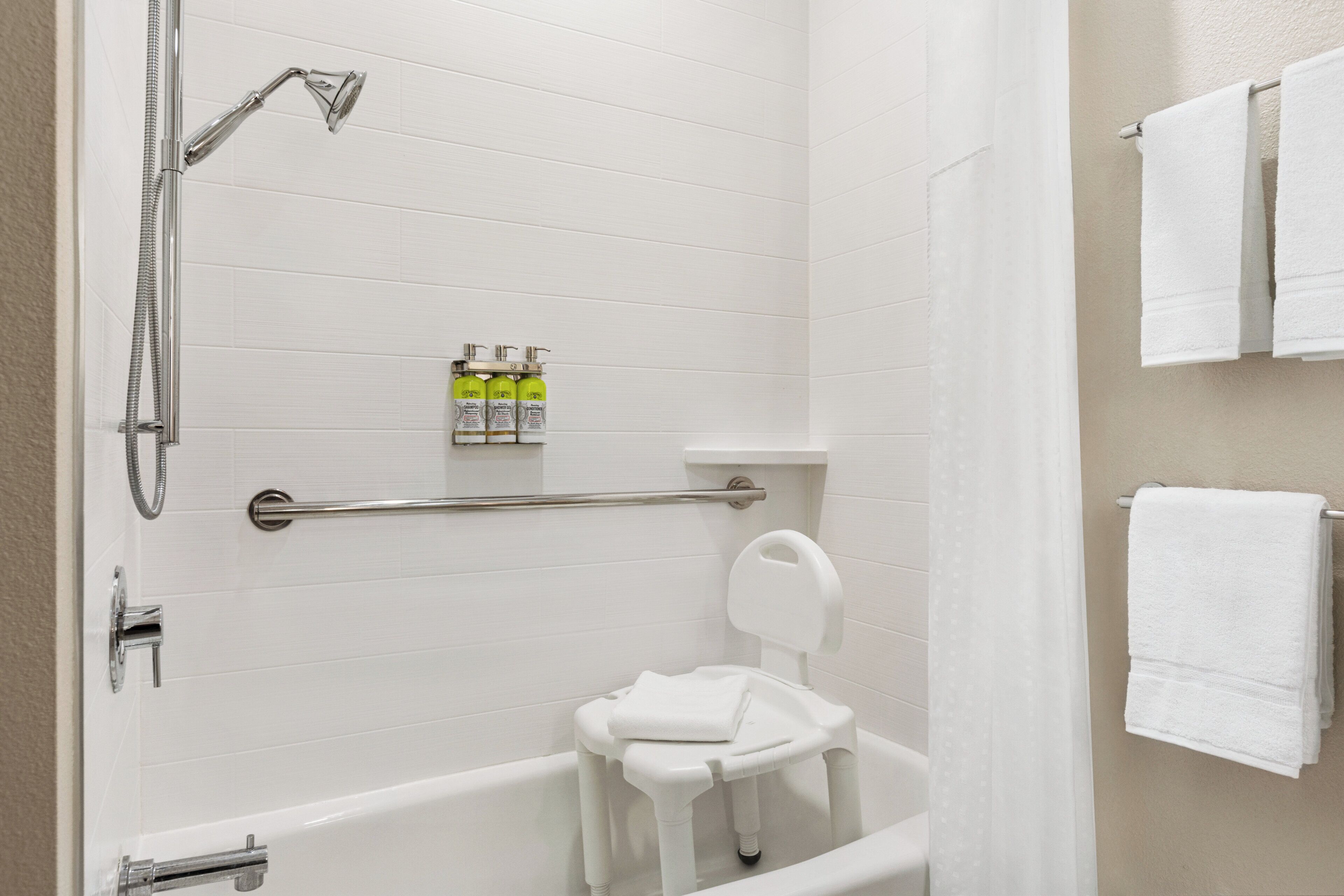 A bathroom with a white bathtub, a shower, and a toilet. There are three bottles of shampoo and conditioner on the wall.