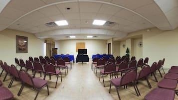 A conference room with rows of chairs, a podium, a television screen, and a clock on the wall.