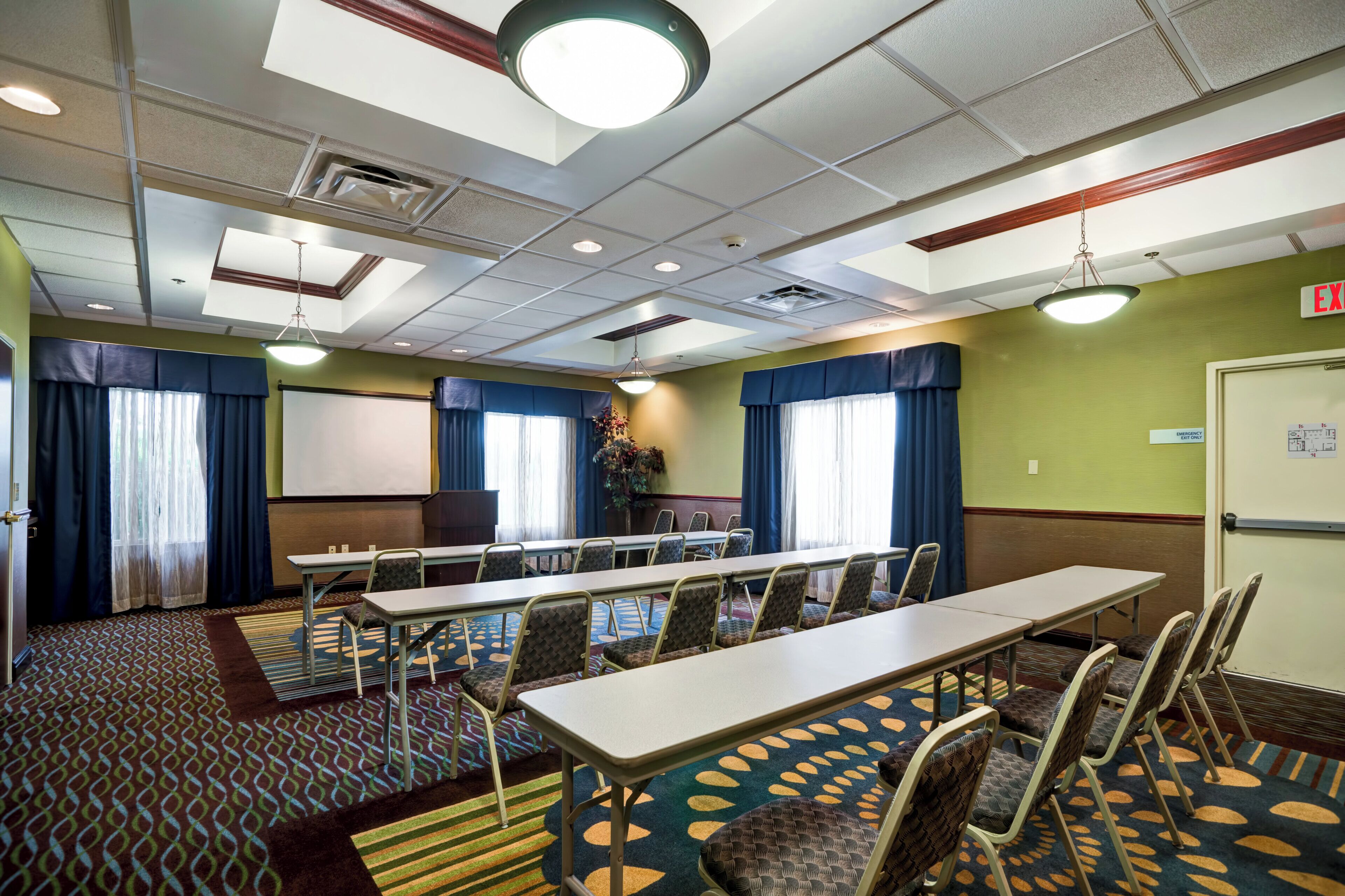 A conference room with a long table, chairs, a projector screen, and a carpeted floor.