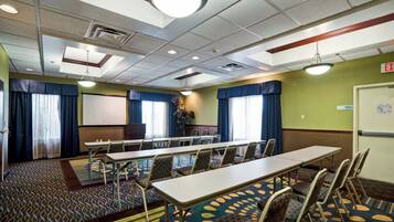 A conference room with a long table, chairs, a projector screen, and a carpeted floor.