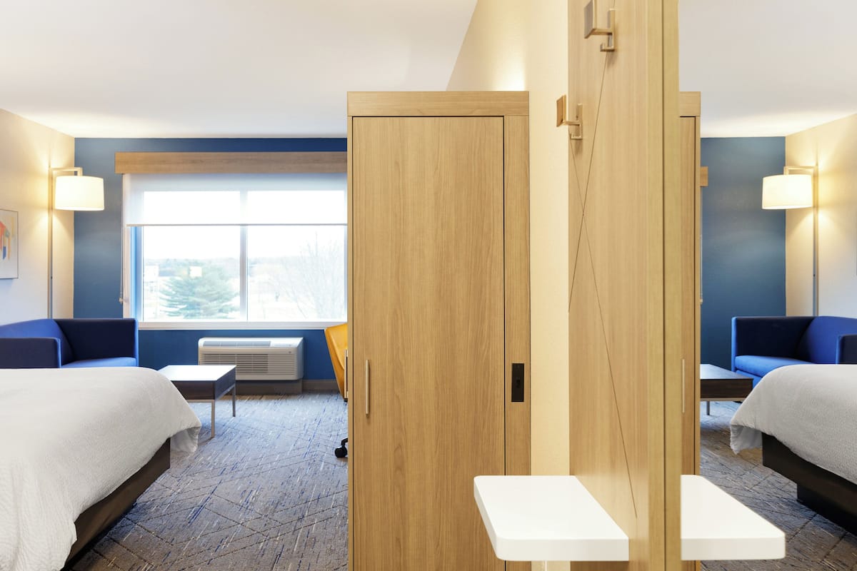 A hotel room with two beds, a small table, and a window with a view.