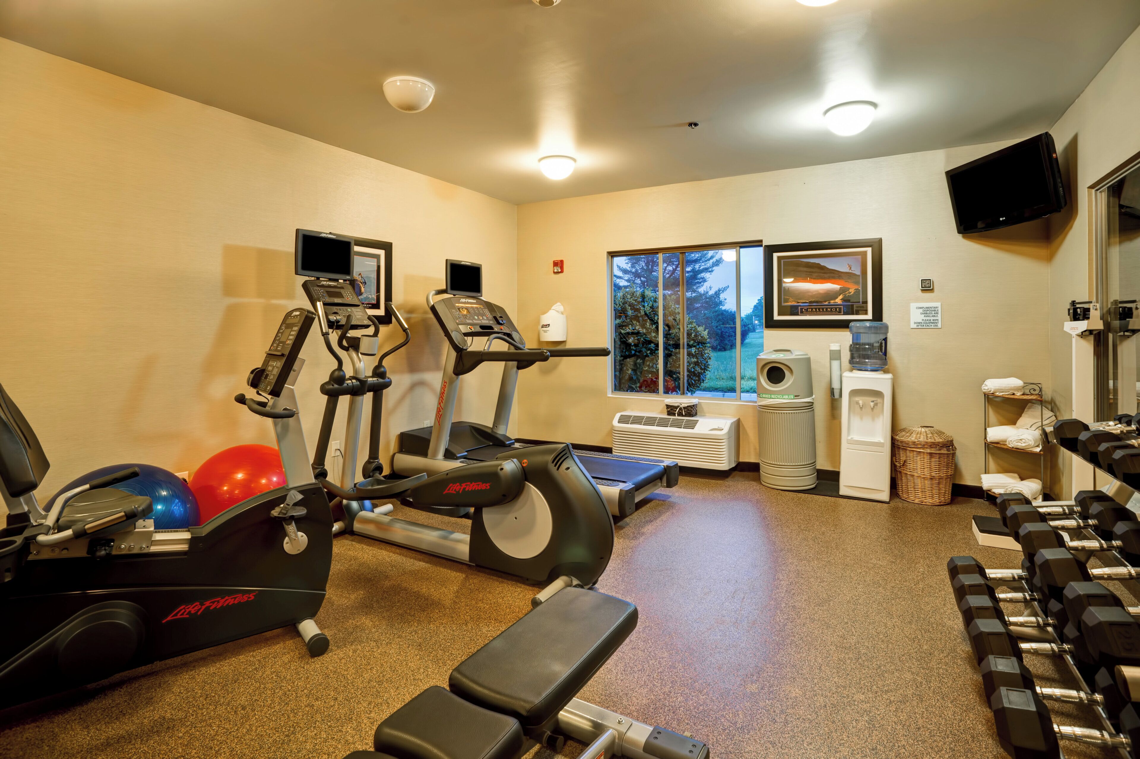 A gym with cardio equipment, dumbbells, and a water dispenser.